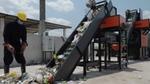 Male worker in overalls and hard hat in a yard, loading waste onto the conveyor belt of a TrashCon sorting and recycling machine.