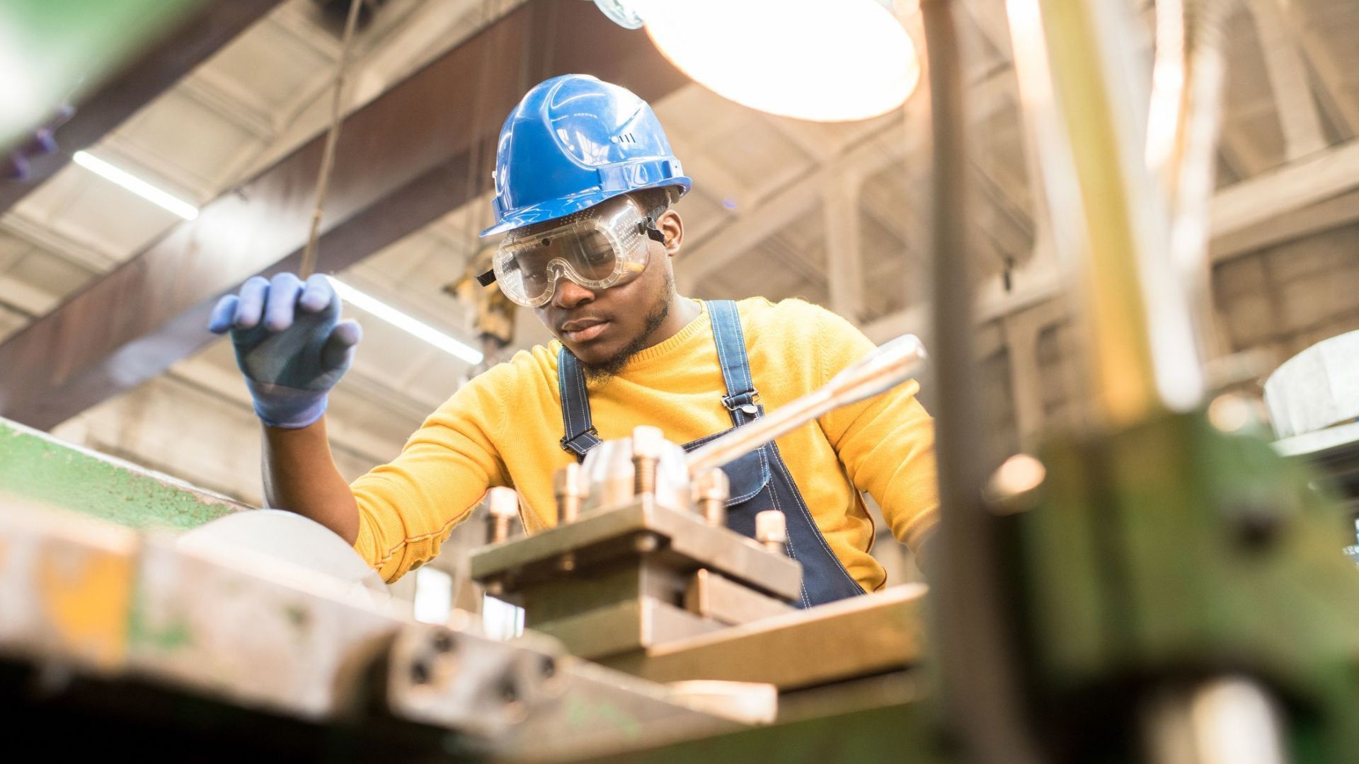 Man wearing hard hat and safety glasses working at a machine in a workshop.