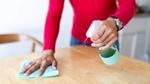 Person using spray bottle and cloth to wipe wooden tabletop. Unilever has developed a fully recyclable spray bottle.