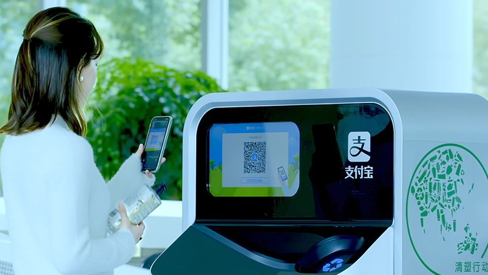 Woman holding plastic bottle ready to scan its QR code into an AI-enabled recycling and sorting machine.