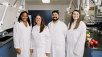 Four Unilever scientists in white lab coats look at camera and smile.