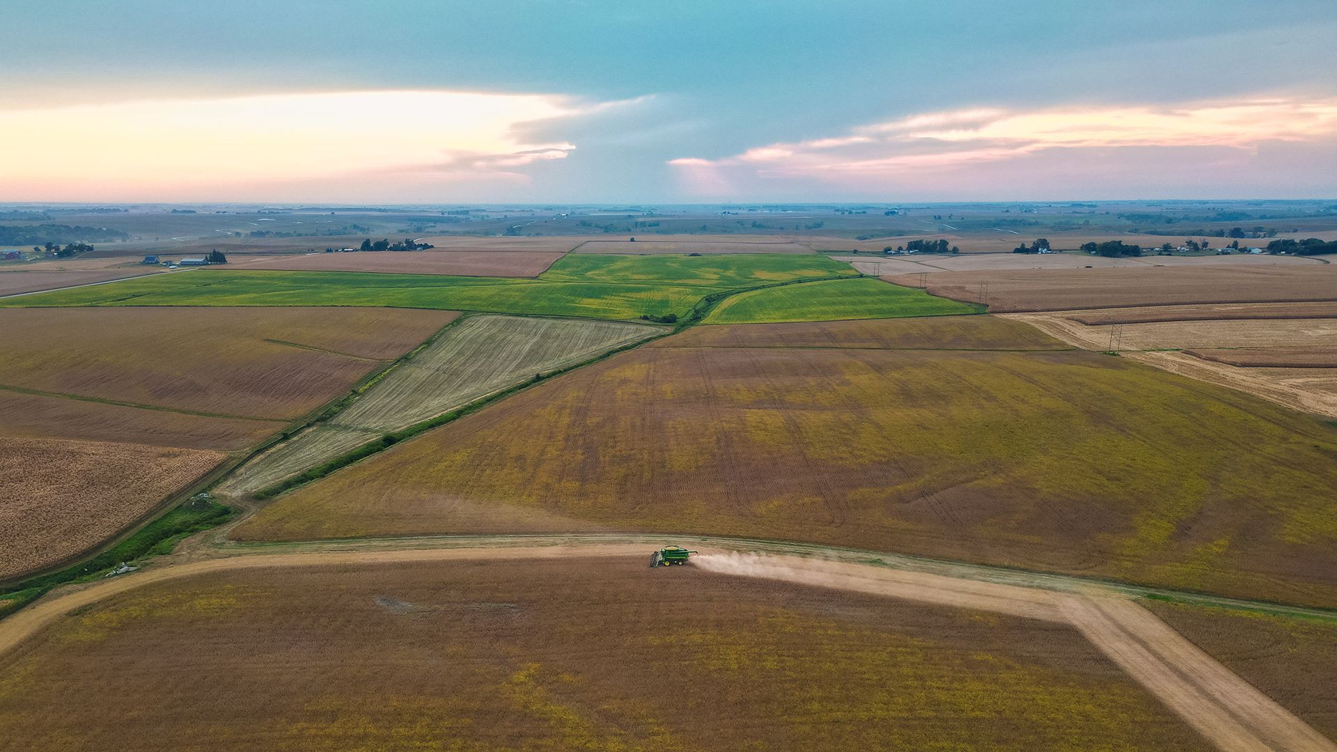 Aerial view of expansive farmland with green and brown fields under a cloudy sunset sky.