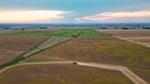 Aerial view of expansive farmland with green and brown fields under a cloudy sunset sky.