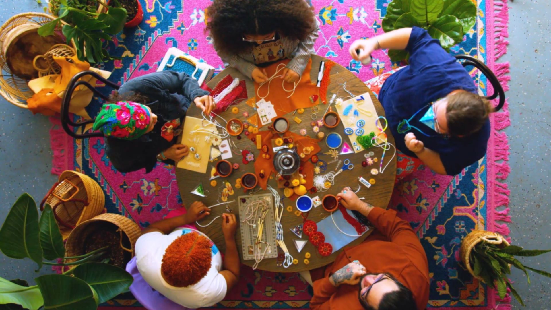 Bird's-eye view of a round table with crafts on top and five people sitting around it.