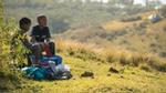 Two boys sit in a field washing clothes over a basin with soap and water