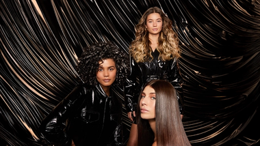 Three women with shiny hair, one blonde waves, one dark curls, one dark glossy. Photo is an ad for TRESemmé Lamellar Shine.
