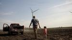 A man in a baseball cap holds the hand of a little girl while walking across a ploughed field to a pick-up truck.