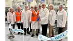 A group of people gather near a manufacturing line. They use a large pair of scissors to cut a blue ribbon that says Unilever and Liquid I.V.