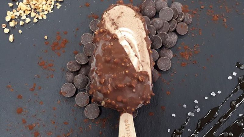 New Vegan Hazelnut Crunch stick sitting on a dark table surrounded by dark chocolate chips